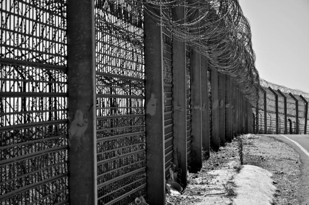 Barbed wire fence along a snowy path in black and white.