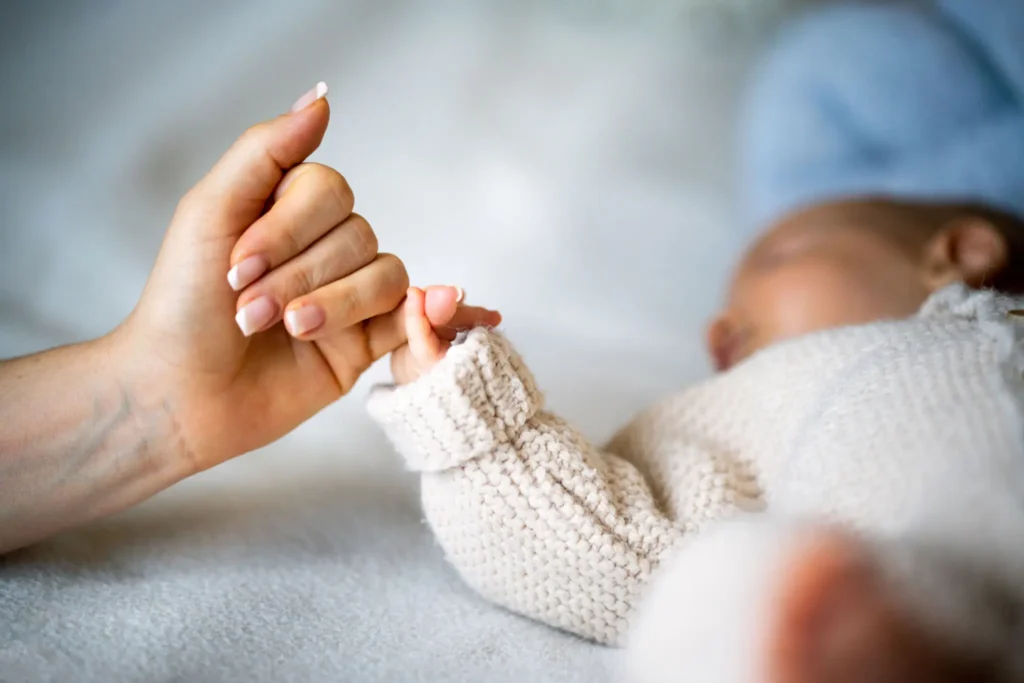 Adult holding a newborn baby's hand gently.
