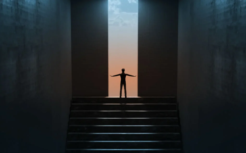 Person standing with arms outstretched between large walls at sunset.