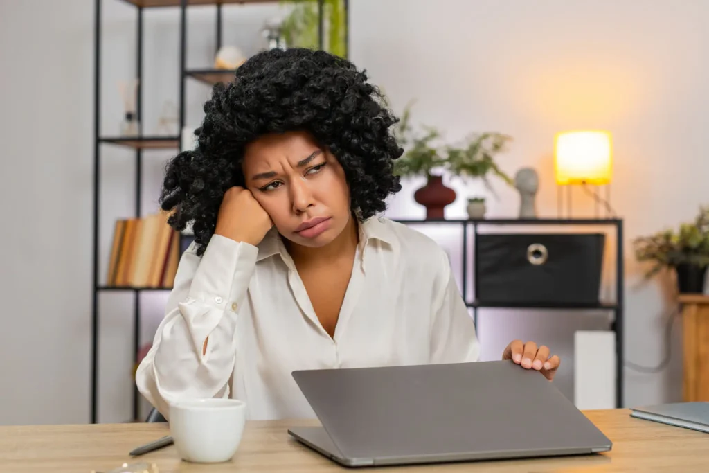 Tired woman sitting at desk with laptop and coffee.